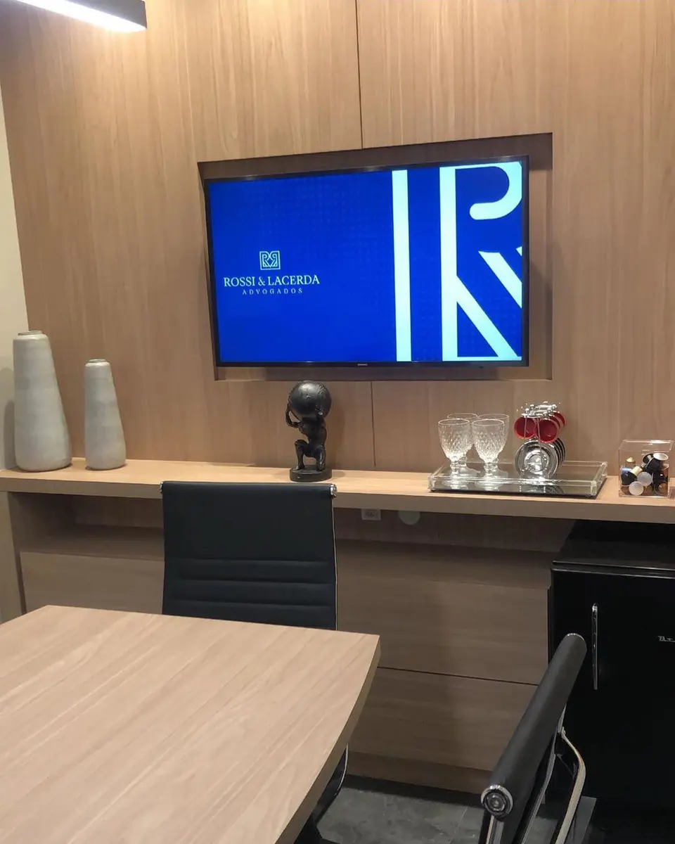 Sala de reunião do escritório com mesa de madeira e tela com o logo